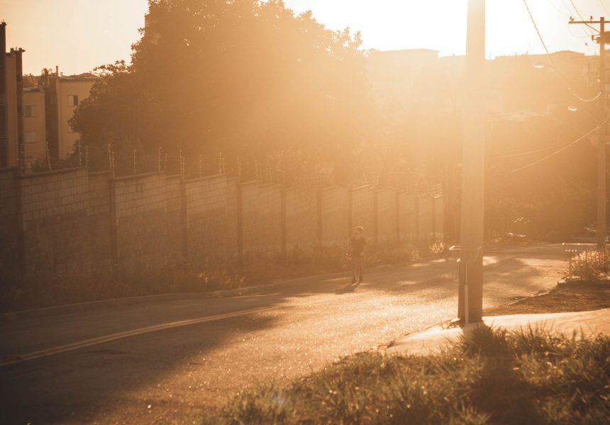 Pessoa caminhando por uma estrada ensolarada durante o fim da tarde, com sombras longas projetadas no asfalto.