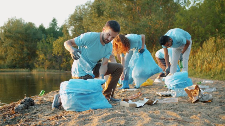 Grupo de voluntários recolhe lixo às margens de um rio usando luvas e sacos para preservar o ambiente.