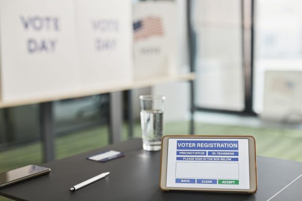 Tablet exibindo um formulário de registro eleitoral em uma estação de votação interna, com sinalização sobre o dia da eleição.