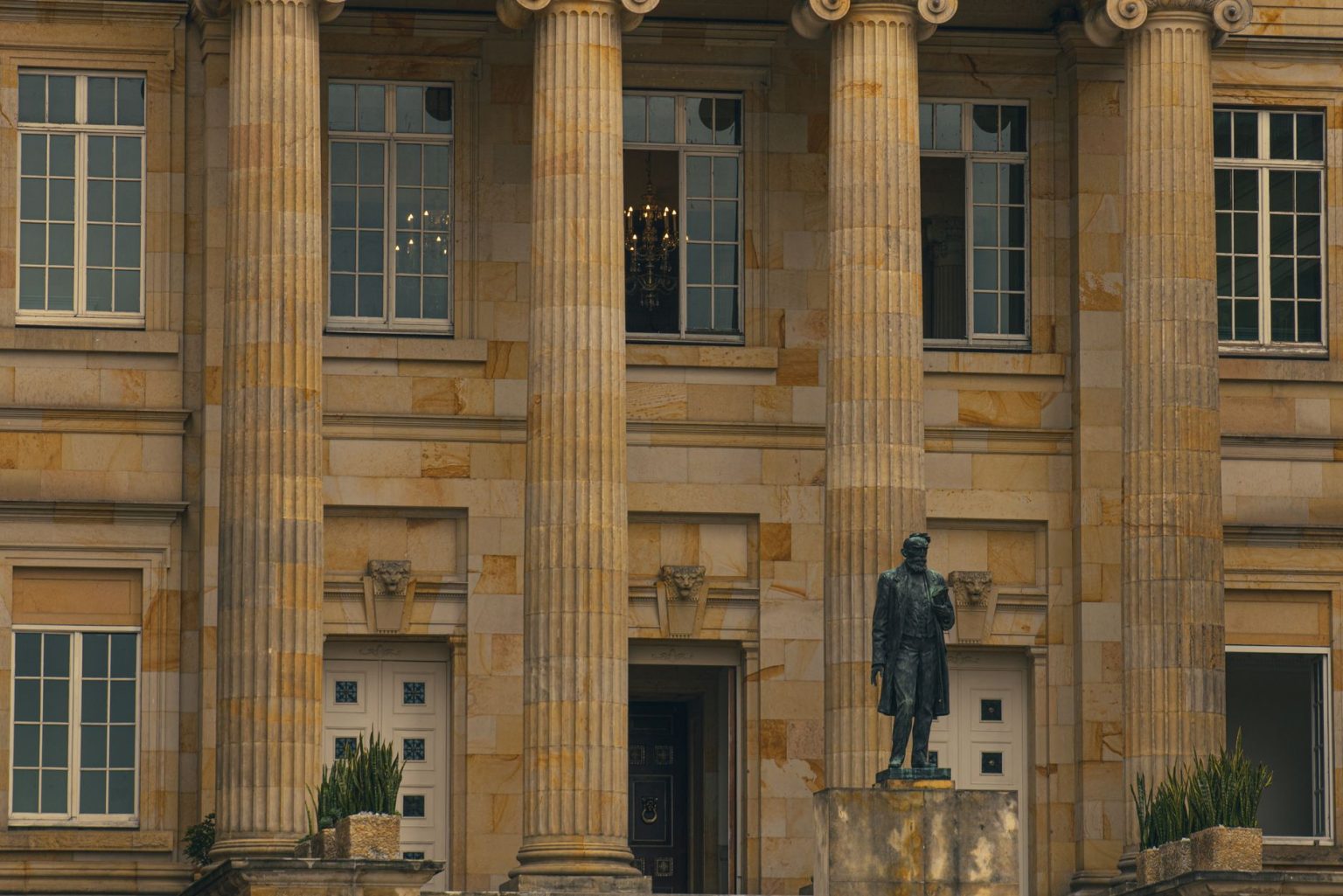 Fachada de um prédio institucional com colunas e uma estátua na entrada.