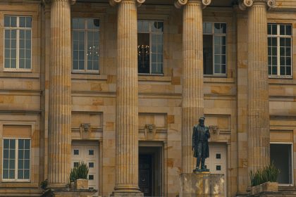 Fachada de um prédio institucional com colunas e uma estátua na entrada.