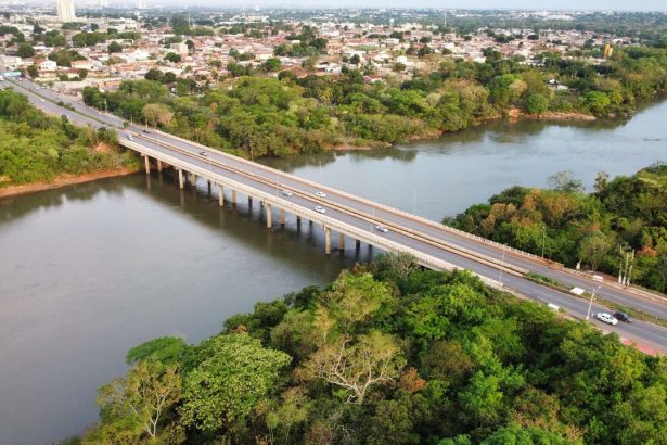 Vista aérea de uma ponte sobre um rio, cercada por áreas verdes, em Cuiabá (MT).