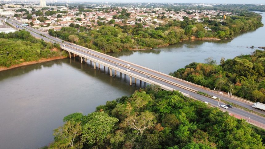 Vista aérea de uma ponte sobre um rio, cercada por áreas verdes, em Cuiabá (MT).