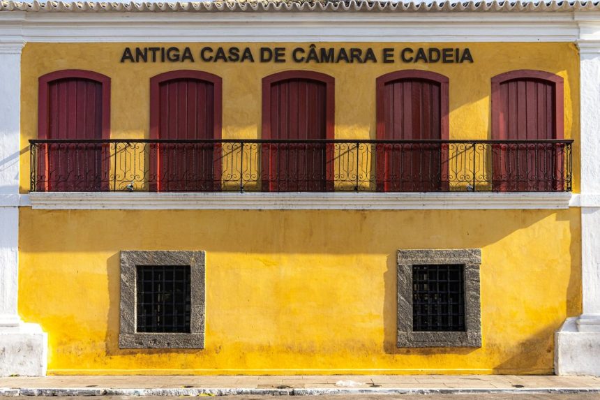 Fachada amarela de um edifício histórico brasileiro, com detalhes arquitetônicos e janelas altas.