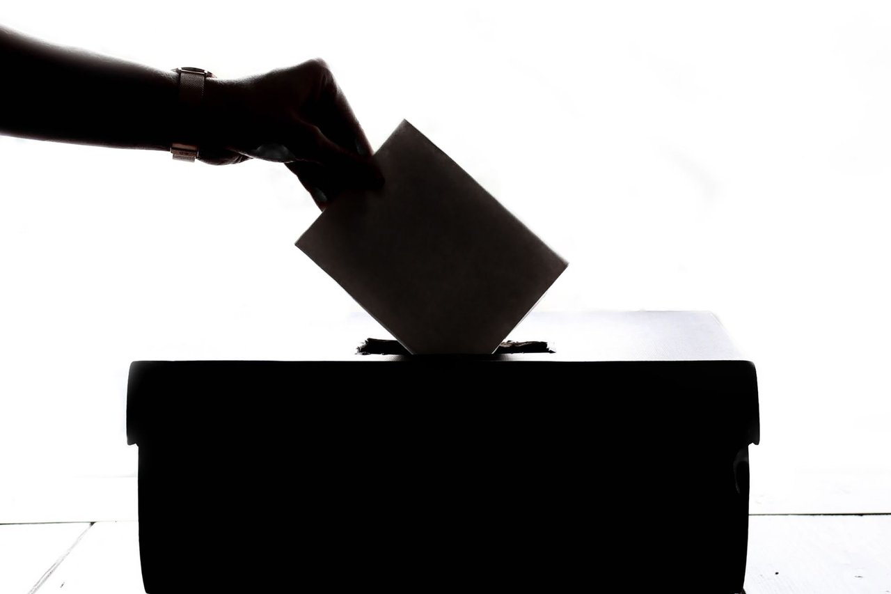 Mão deposita um voto em uma urna, em uma representação genérica do processo eleitoral.